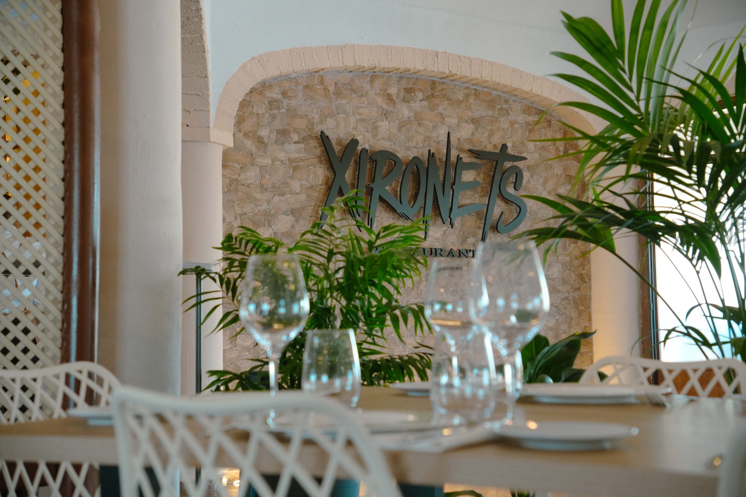 Detalle de una mesa de Xironets, con copas y el logotipo del restaurante al fondo